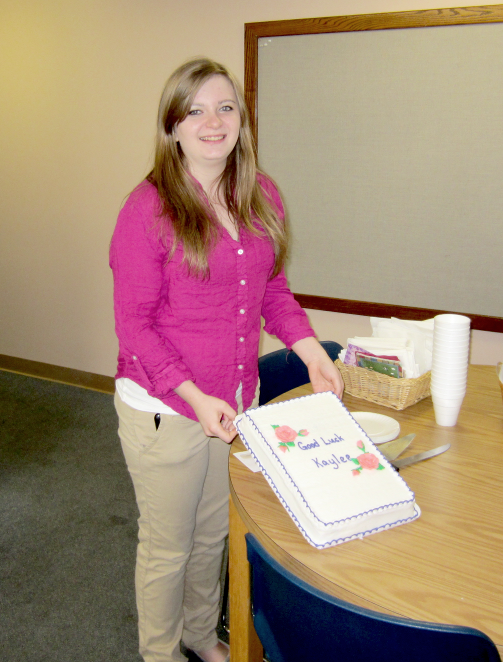 [photo - young woman holding a cake, which reads Good Luck Kaylee]