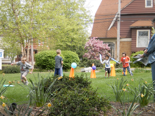 [photo of four boys playing in the yard with foam noodles, balls, and traffic cones]