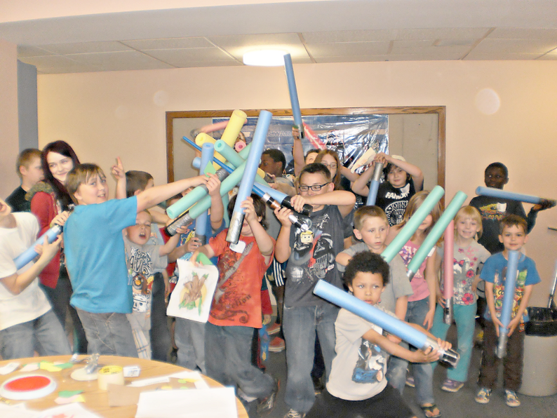 [photo of a group of kids playing light saber with foam noodles]